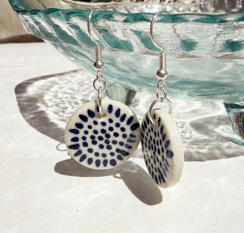 Pair of earrings with circular designs hanging against a textured surface