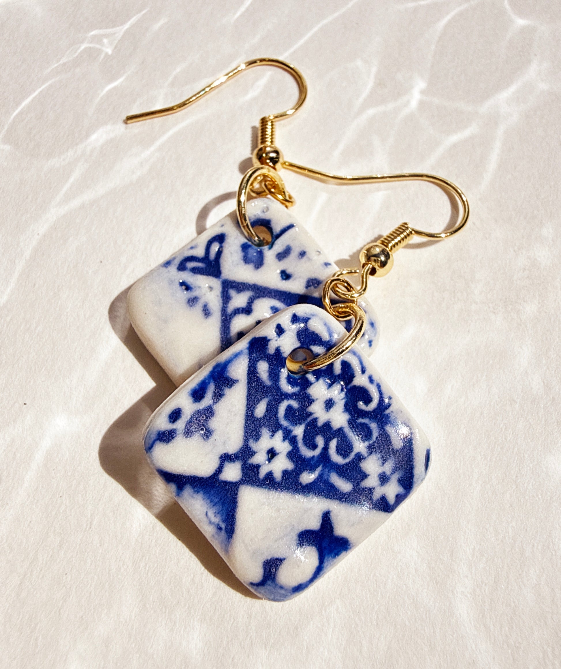 Handmade porcelain Earrings with blue and white patterned stones on a beige background
